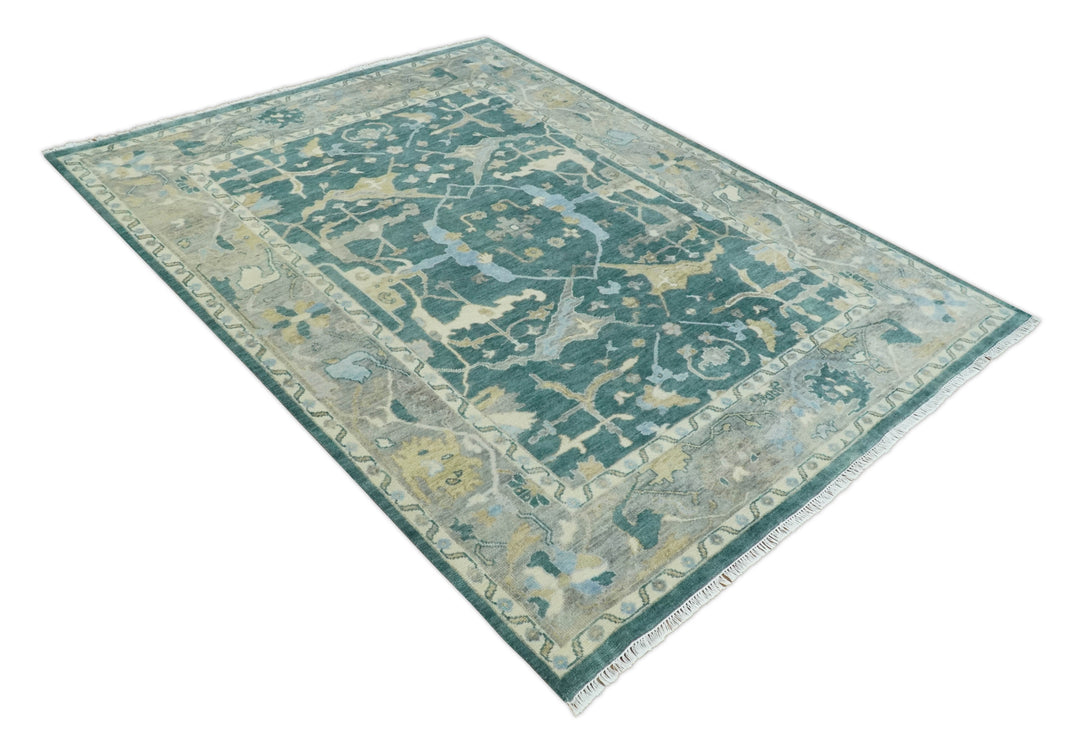 Teal and beige Oushak rug with geometric motifs, shown diagonally with fringed corners.