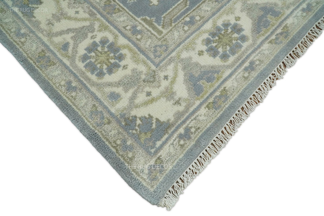 Corner of blue-gray and ivory traditional rug with short fringe edging.