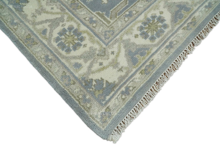 Corner of blue-gray and ivory traditional rug with short fringe edging.