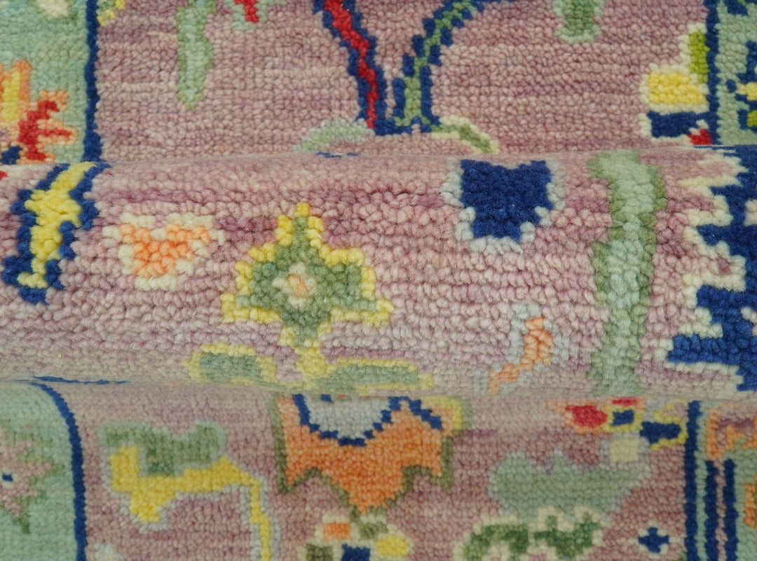 Close-up of Traditional Oushak wool rug with pastel pink pile and scattered colorful motifs