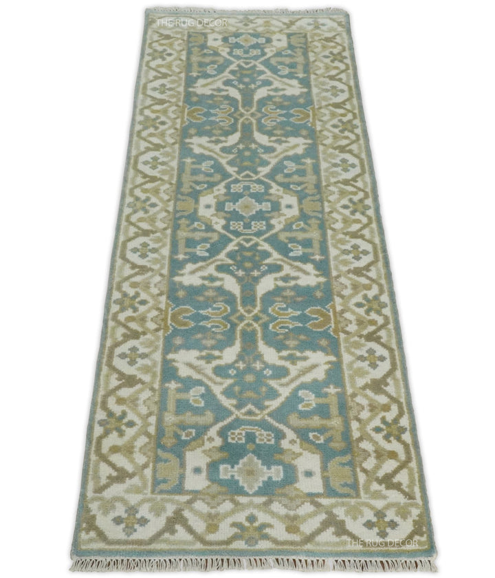 Full view of the rug's ornate teal center, ivory border, and fringed ends