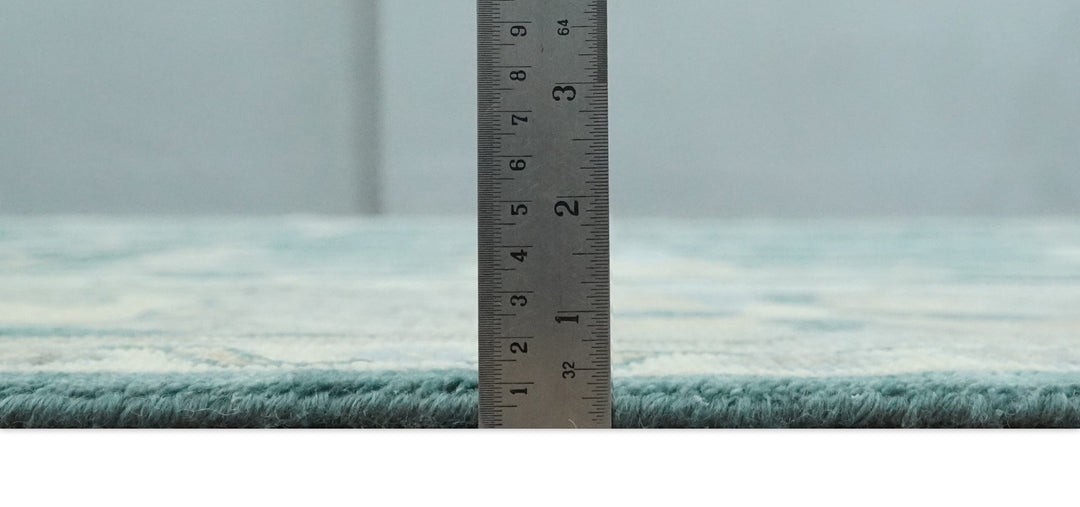 Teal and beige rug edge with measuring tape showing pile height near the border.