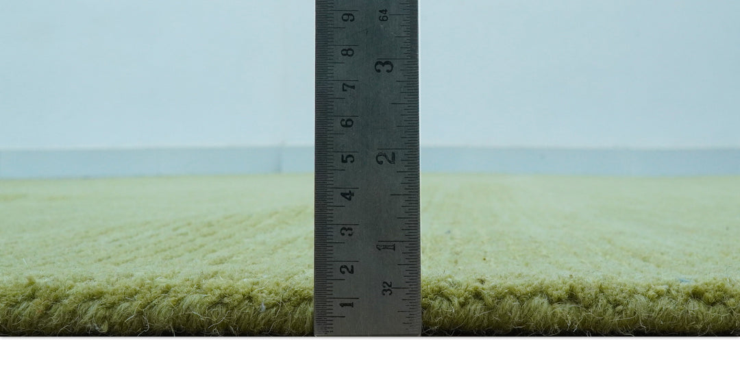 Side view of the rug's thick green wool pile beside a ruler