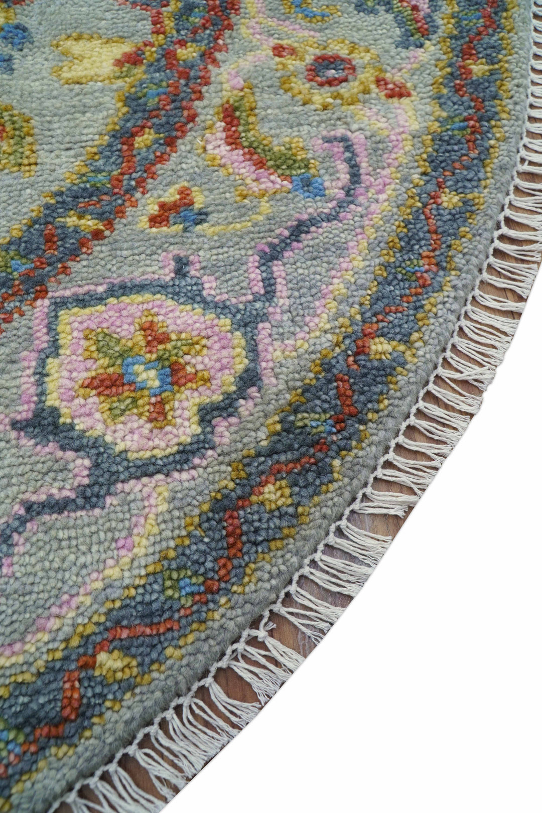 Diagonal view of multicolor round wool rug with decorative border and fringe trim