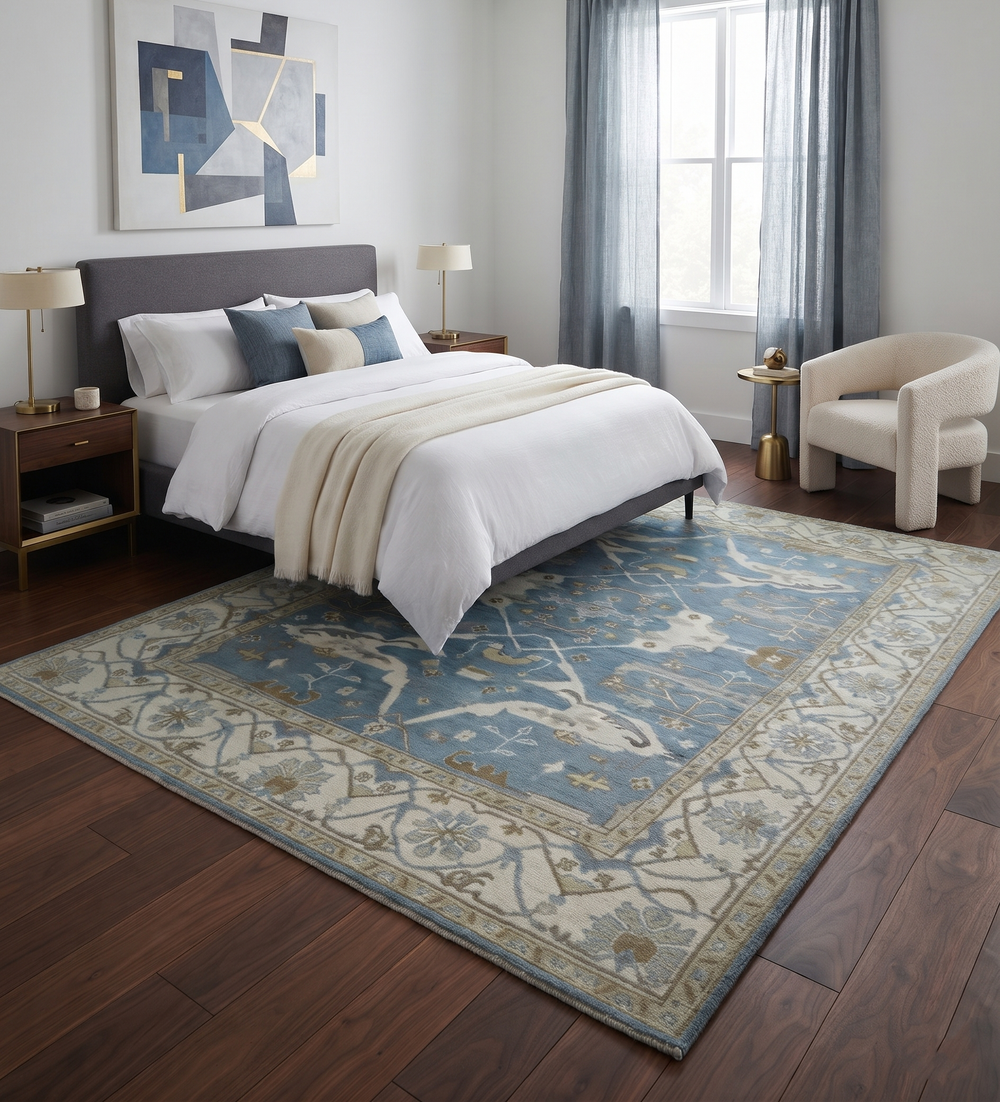 Blue and ivory Oushak wool rug displayed beneath a bed, showing its floral pattern and wide border