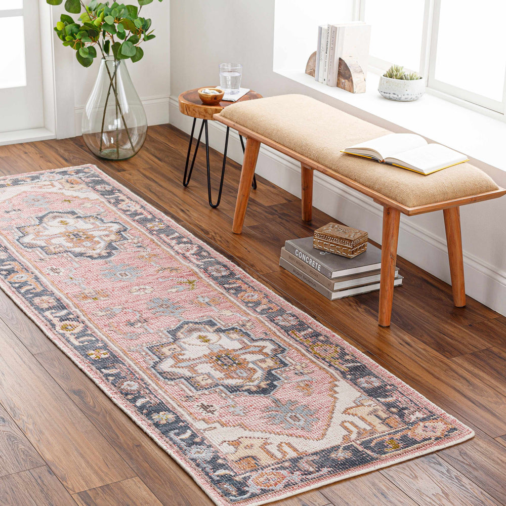 Pink and blue ornate traditional area rug laid along wood floor in a room setting