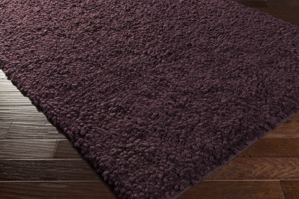 Hand woven wool area rug, dark purple, angled corner view showing thick looped pile.