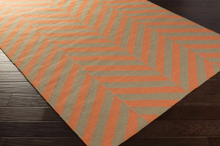 Hand-woven area rug corner view with orange chevron stripes on cream and tan