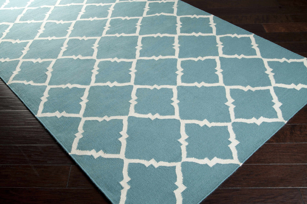 Blue area rug with white trellis quatrefoil pattern, shown folded diagonally