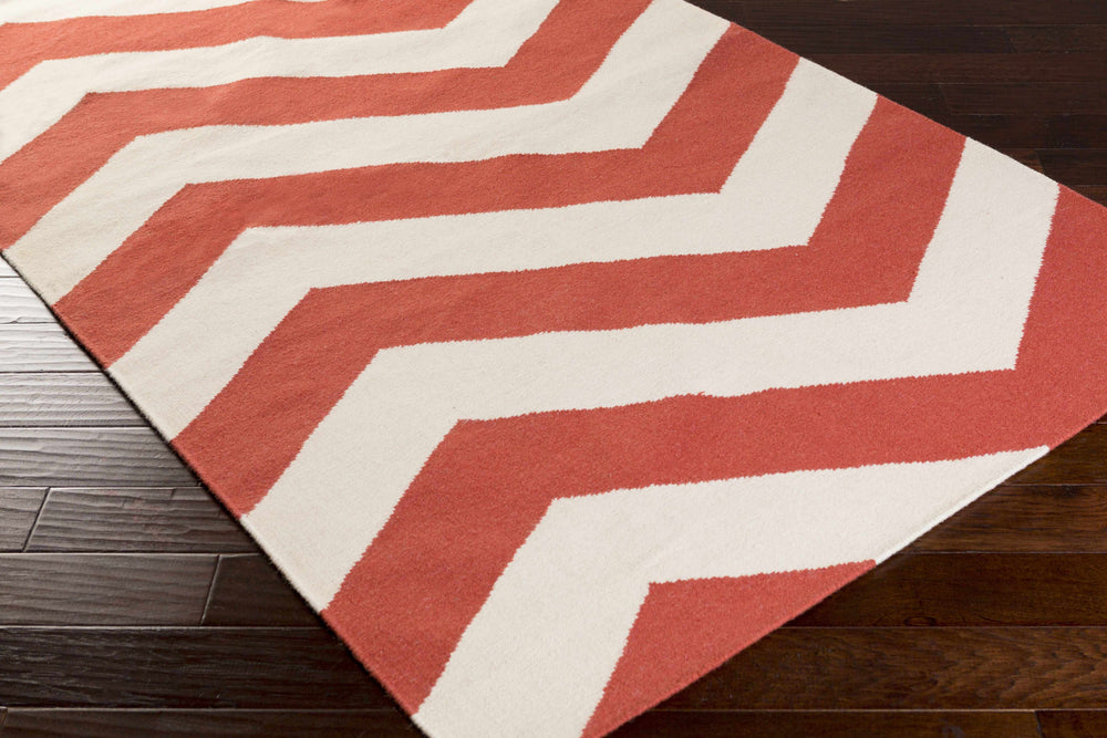 Rust and ivory chevron area rug laid on wood floor, corner view.