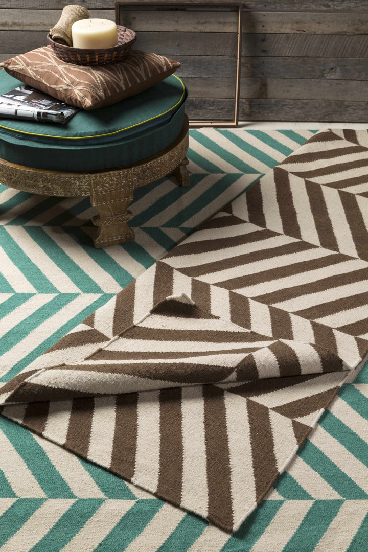 Chevron patterned area rug in green and cream, styled with cushions on it.