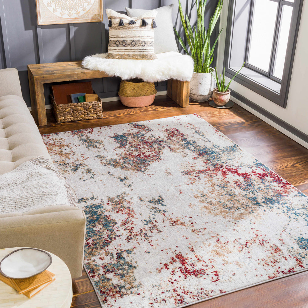 Multicolor abstract area rug in a room, cream base with blue and red speckled design.