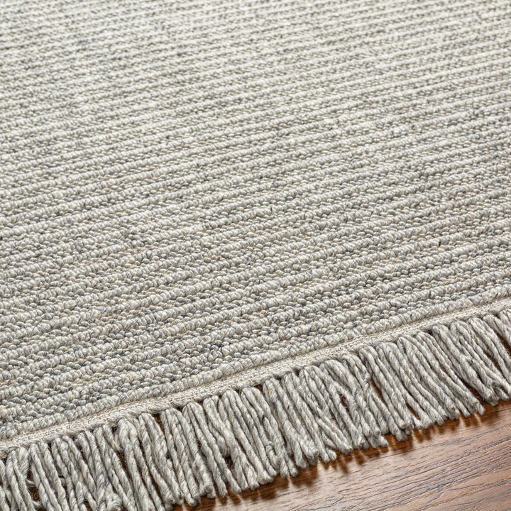 Close-up of a textured rug with fringe on a wooden floor