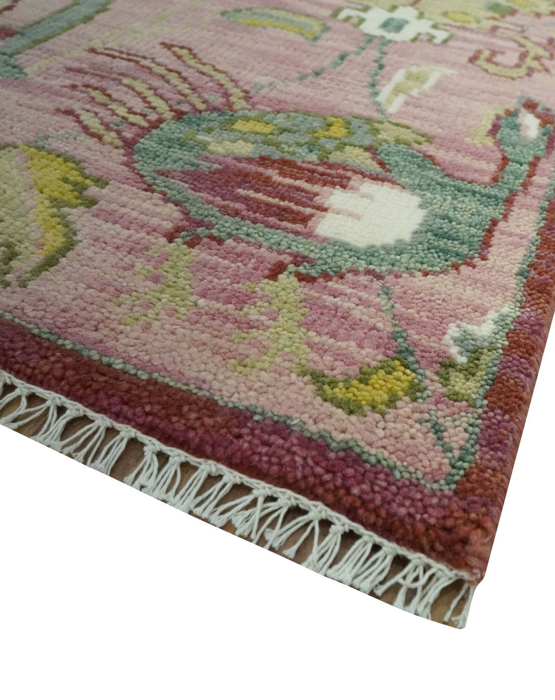 Corner of pink and green hand-knotted wool rug with fringe and multicolor motifs