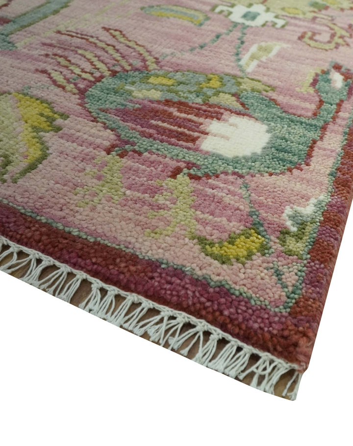 Corner of pink and green hand-knotted wool rug with fringe and multicolor motifs