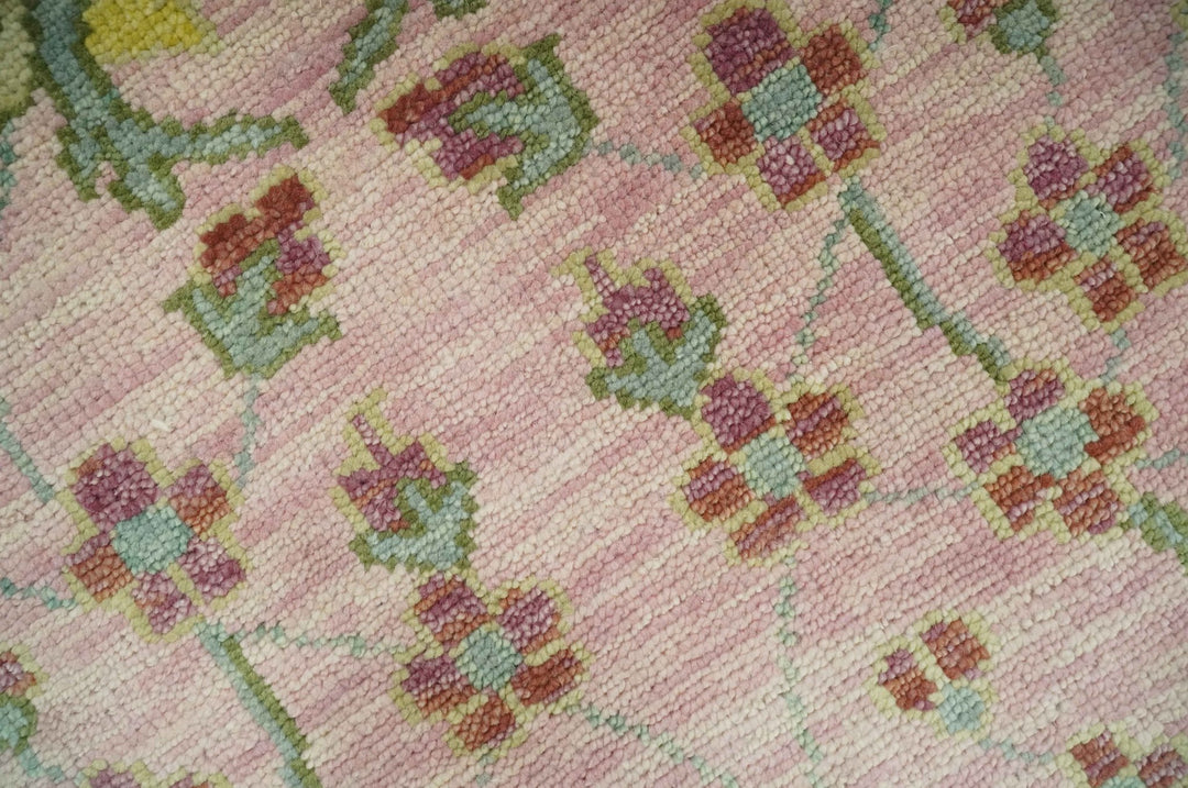 Hand-knotted wool rug texture close-up with pink ground and green floral pattern