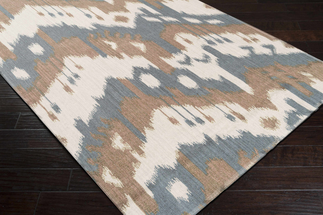 Abstract patterned area rug corner with cream, blue, and beige tones on dark floor