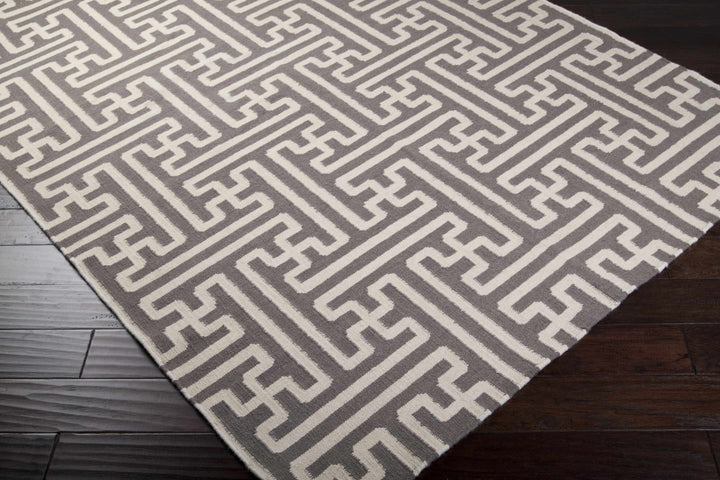 Gray and ivory Greek-key area rug with corner edges visible on dark wood floor
