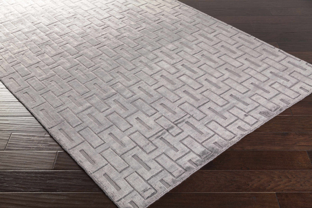 Gray and silver geometric area rug corner on wood floor, interlocking brick design