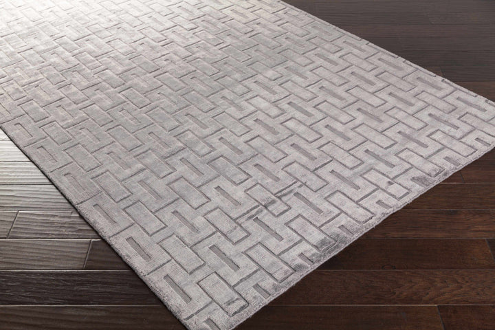 Gray and silver geometric area rug corner on wood floor, interlocking brick design