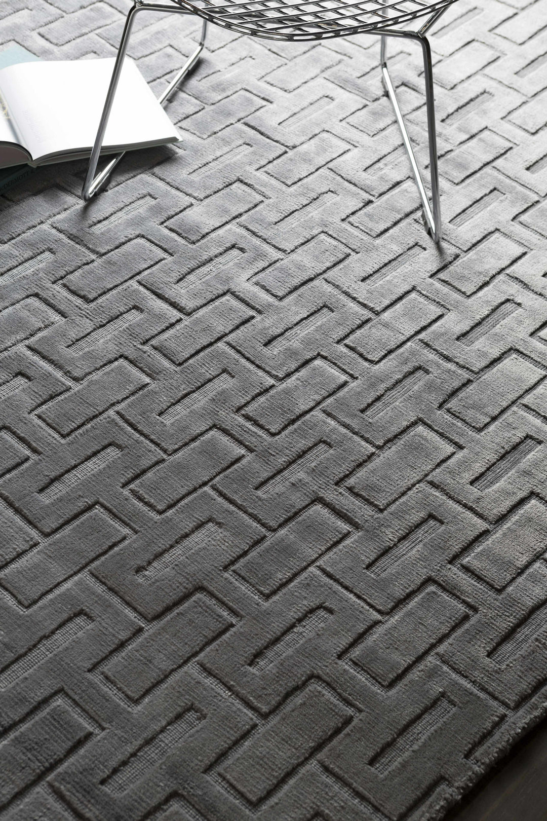Gray and silver geometric area rug with chevron brick pattern, corner fold visible
