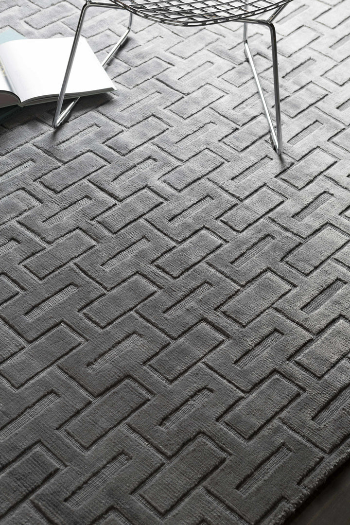 Gray and silver geometric area rug with chevron brick pattern, corner fold visible