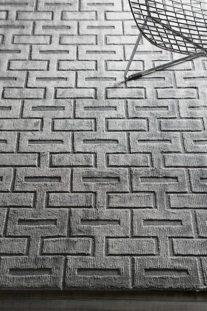 Silver and gray geometric area rug with raised brick pattern, curled corner on floor