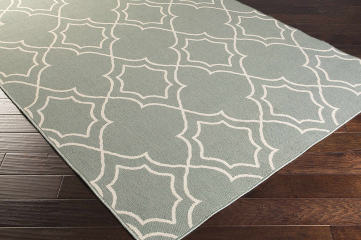 Corner view of green area rug with beige geometric trellis quatrefoil pattern